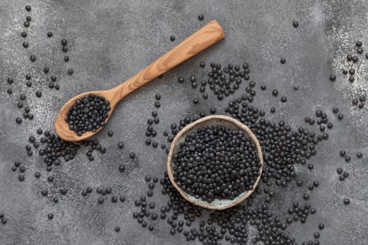 Bowl and spoon of black beluga lentils beans on grey table top view. Healthy eating, protein source for vegan and vegetarian diet. Traditional Asian and North African cuisines ingredient