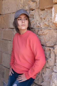 Teen girl wearing pink long sleeve shirt and baseball cap looking aside. Mockup. Serious Teenager girl standing outdoor near a wall, spending her time alone. Adolescence concept