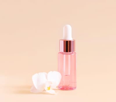 Light Pink Dropper Bottle near white orchid flower on light yellow, close up, mockup. Skincare beauty product, Aromatic oil or serum. Exotic cosmetics, pastel minimal composition..