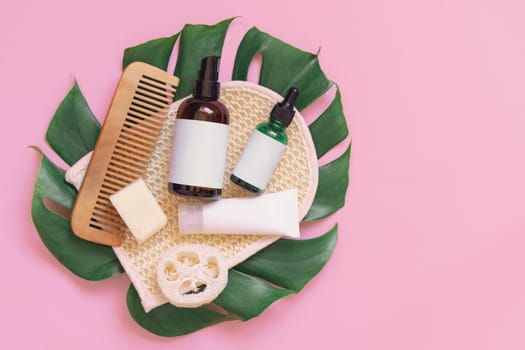 Homemade Cosmetics and eco friendly accessories on monstera leaf on pink flat lay, copy space. Brand packaging mockup. Natural beauty products for hair and skin care, Top view