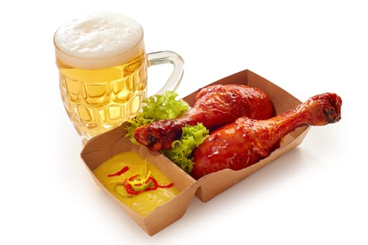 High angle of yummy BBQ chicken legs in sauce and mustard in paper container placed with glass of cold beer on white isolated background