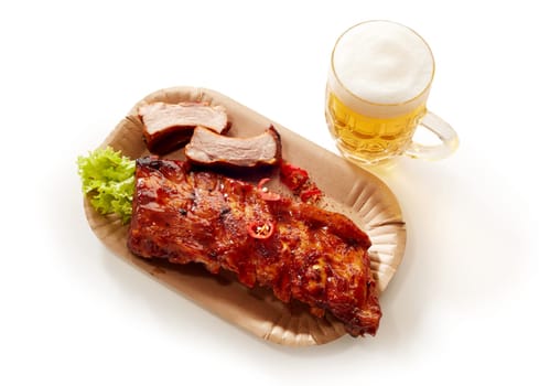 From above of appetizing barbeque pork spare ribs on plate and mug of cold beer served on white isolated background