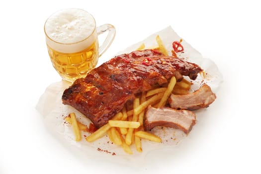 High angle of appetizing barbeque pork spareribs and French fries served on plate on table with glass of cold lager beer on white background in studio