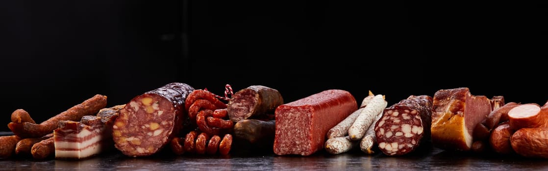 Assorted types of tasty dry cured sausages with appetizing smoked lard served on table on black background in modern studio