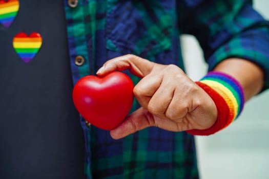 Asian woman holding red hert with rainbow flag, LGBT symbol rights and gender equality, LGBT Pride Month in June.