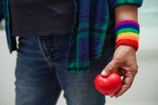 Asian woman holding red hert with rainbow flag, LGBT symbol rights and gender equality, LGBT Pride Month in June.