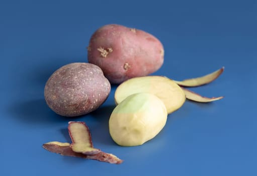 Raw peeled red potato tubers on blue table close up. Vegetarian diet. Carbohydrates. Minimnal composition