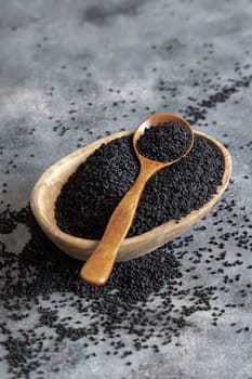 Indian spice Black cumin (nigella sativa or kalonji) seeds in bowl with spoon on grey table close up with copy space. Traditional medicine, healthy and vegetarian food concept.