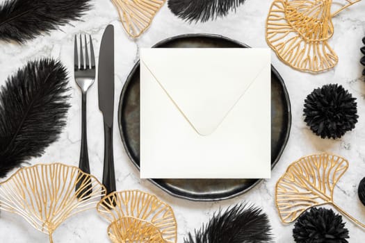 Black and golden wedding table setting with a blank square envelope top view, mockup. Elegant modern holiday flat lay, wedding or holiday stationery template