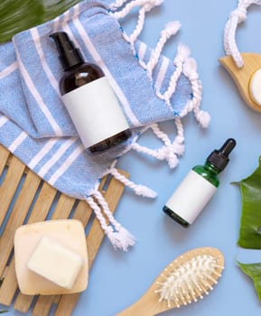 Glass one pump dispenser, skin and hair care accessories on blue bath towel top view, copy space. Packaging mockup. Natural homemade products