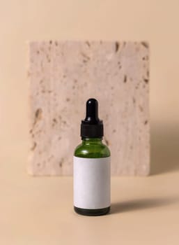 Green glass dropper bottle near beige travertine stone on light yellow, close up, mockup. Skincare beauty product, serum or lotion. Handmade natural cosmetics, trendy minimal composition..