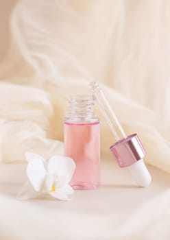 Light Pink opened Dropper Bottle near white orchid flower on light yellow, close up, mockup. Skincare beauty product, Aromatic oil or serum. Exotic cosmetics, pastel composition..