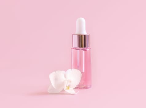 Light Pink Dropper Bottle near white orchid flower on light pink ,close up, mockup. Skincare beauty product, Aromatic oil or serum. Exotic cosmetics, pastel minimal composition..