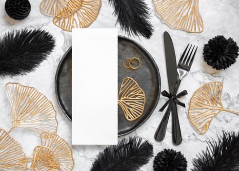 Black and golden wedding table setting with a blank card and rings top view, mockup. Elegant flat lay with vertical menu or Invitation paper card, wedding or holiday stationery template