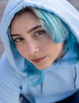 Blue haired Teenage girl in light blue oversize hoodie and looking into the camera from down. Blue haired teen girl outdoor.