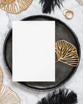 Black and golden wedding table setting with a blank card top view, mockup. Elegant flat lay with vertical greeting or Invitation paper card, wedding or holiday stationery template
