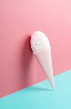 Ice cream cone with an egg, pink and blue background, copy space, easter holiday, summer season, minimalism and creative concept, greeting card