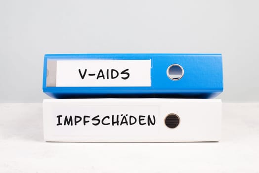 The words v-aids and vaccine damage are standing in german language on folders, new autoimmune disease caused by covid-19 syringe, immune system injury, health issue