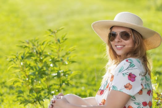 Summer portrait of smiling attractive  young woman in straw hat posing outdoors. Horizontally.