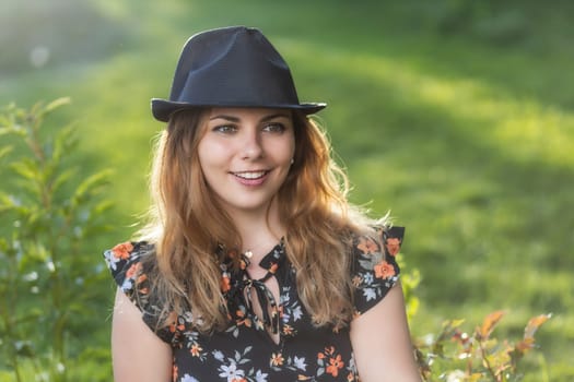 Portrait of attractive  smiling young woman in black  straw hat posing outdoors . Horizontally.