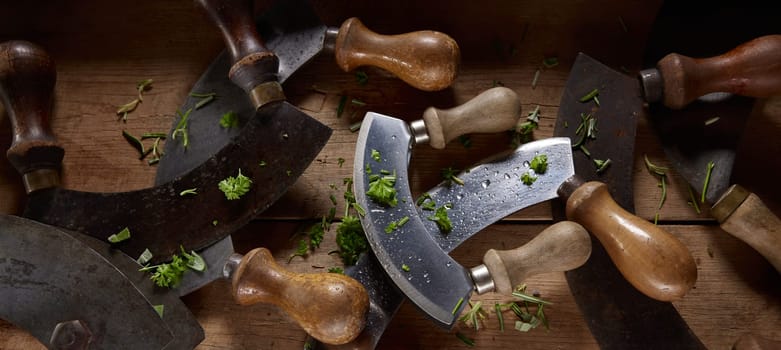 From above of old fashioned Mezzaluna knives with wooden handles covered with chopped greens and placed on table in kitchen