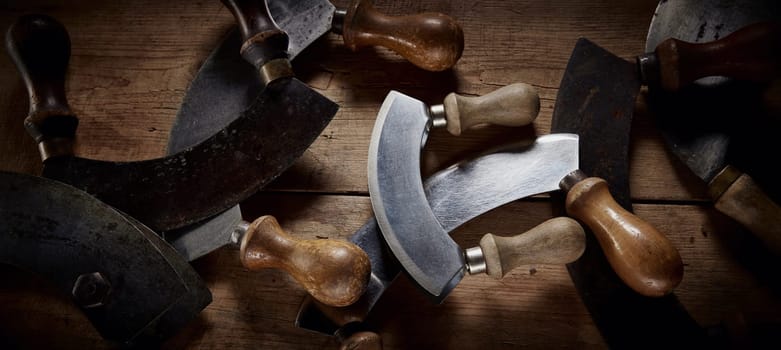 Top view of collection of old fashioned mezzaluna knives with curved blades and wooden handles placed on table in kitchen