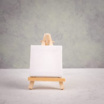 Easel with blank white canvas in front of a gray textured background, frame to add paintings and pictures