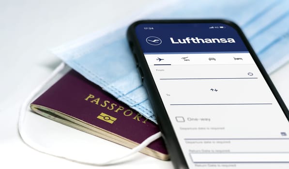 Berlin, GER, MAY 2022: phone with the Lufthansa airlines mobile app on the screen lying over a protective mask and a passport. Travel safety and restrictions during coronavirus pandemic