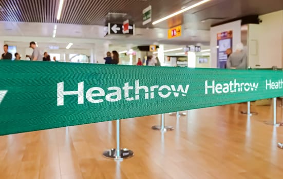 London, UK, May 2022: Green belt barrier with white London Heathrow International Airport logo. American Airlines is a major US-based airline. Travel and airport security