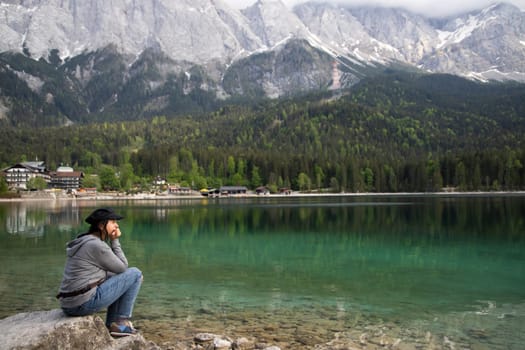 Tourist sitting on a rock and watching a beautiful view over lake Eibsee in the Bavarian Alps. Famous touristic destination in Europe