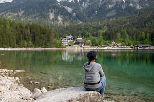 Tourist sitting on a rock and watching a beautiful view over lake Eibsee in the Bavarian Alps. Famous touristic destination in Europe