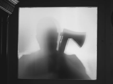 Horror, halloween background - Shadowy figure behind glass of a man holding an axe