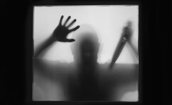 Horror, halloween background - Shadowy figure behind glass of a man holding a knife