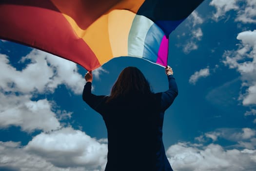 Woman sitting in a green meadow holding a Gay Rainbow Flag. Bisexual,gay, lesbian, transsexual symbol. Happiness, freedom and love concept for same sex couples