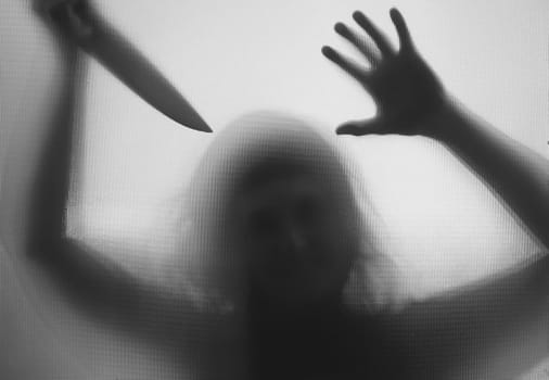 Horror, halloween background - Shadowy figure behind glass holding a knife