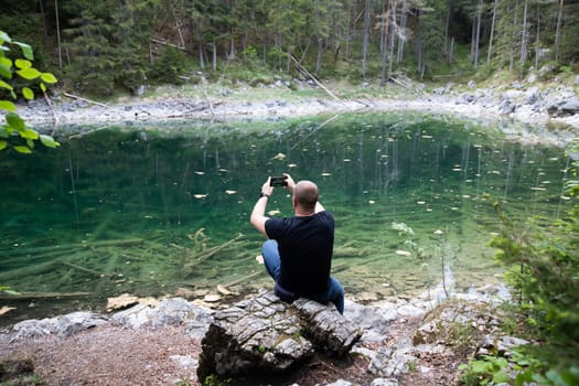 Tourist sitting on a rock and watching a beautiful view over lake Eibsee in the Bavarian Alps. Famous touristic destination in Europe