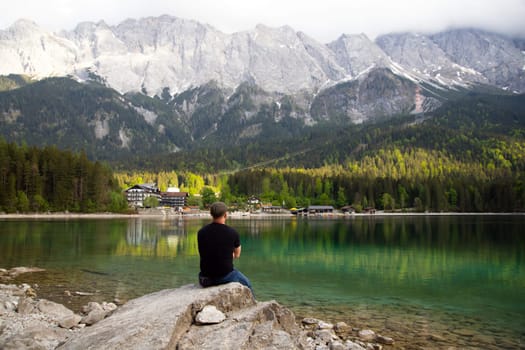 Tourist sitting on a rock and watching a beautiful view over lake Eibsee in the Bavarian Alps. Famous touristic destination in Europe