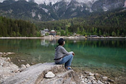 Tourist sitting on a rock and watching a beautiful view over lake Eibsee in the Bavarian Alps. Famous touristic destination in Europe