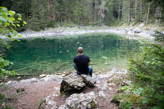 Tourist sitting on a rock and watching a beautiful view over lake Eibsee in the Bavarian Alps. Famous touristic destination in Europe