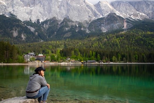 Tourist sitting on a rock and watching a beautiful view over lake Eibsee in the Bavarian Alps. Famous touristic destination in Europe