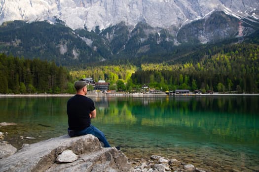 Tourist sitting on a rock and watching a beautiful view over lake Eibsee in the Bavarian Alps. Famous touristic destination in Europe