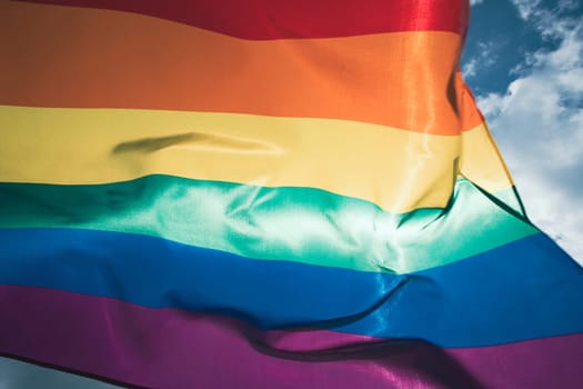 Bright rainbow LGBT flag fluttering against blue sky. LGBT community, happiness, freedom and love concept for same sex couples.