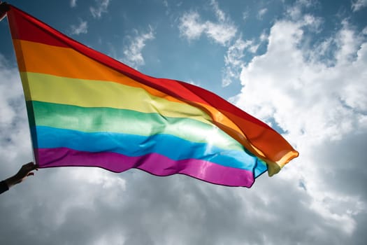 Bright rainbow LGBT flag fluttering against blue sky. LGBT community, happiness, freedom and love concept for same sex couples.