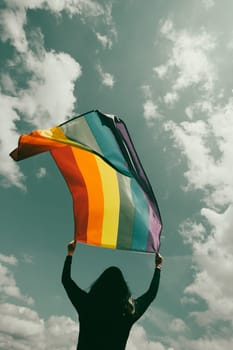 Woman sitting in a green meadow holding a Gay Rainbow Flag. Bisexual,gay, lesbian, transsexual symbol. Happiness, freedom and love concept for same sex couples