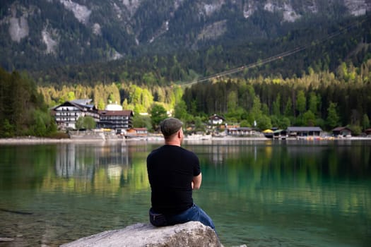 Tourist sitting on a rock and watching a beautiful view over lake Eibsee in the Bavarian Alps. Famous touristic destination in Europe