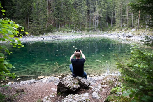Tourist sitting on a rock and watching a beautiful view over lake Eibsee in the Bavarian Alps. Famous touristic destination in Europe