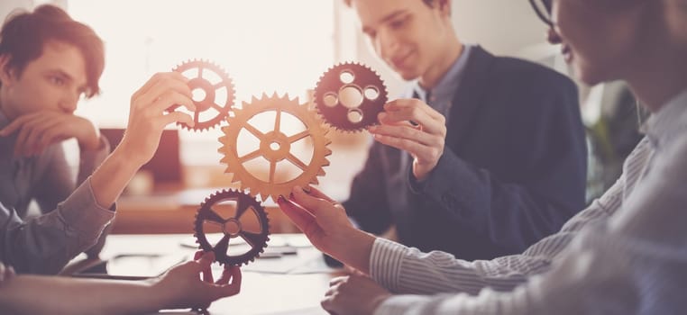 Group of people working in the office while putting together cogwheels. Concept of teamwork and togetherness.