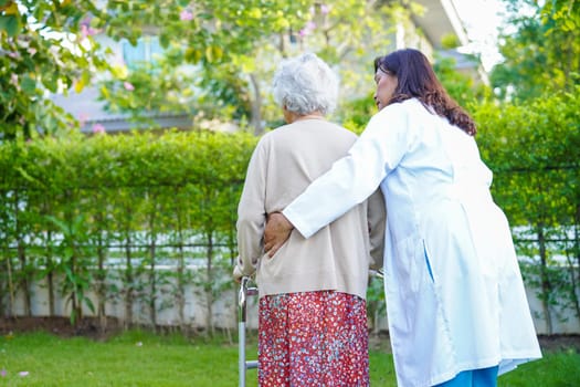 Doctor help Asian elderly woman disability patient walk with walker in park, medical concept.