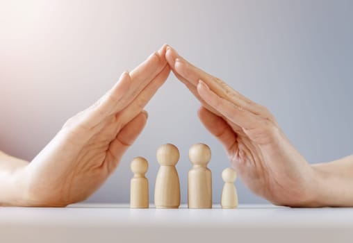 Woman hands under wooden models of family. The concept of helping the people and supporting.