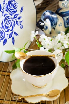 A cup of aromatic black coffee with flowers of cherry on the table. Morning coffee espresso for breakfast with beautiful plate. Vertical image